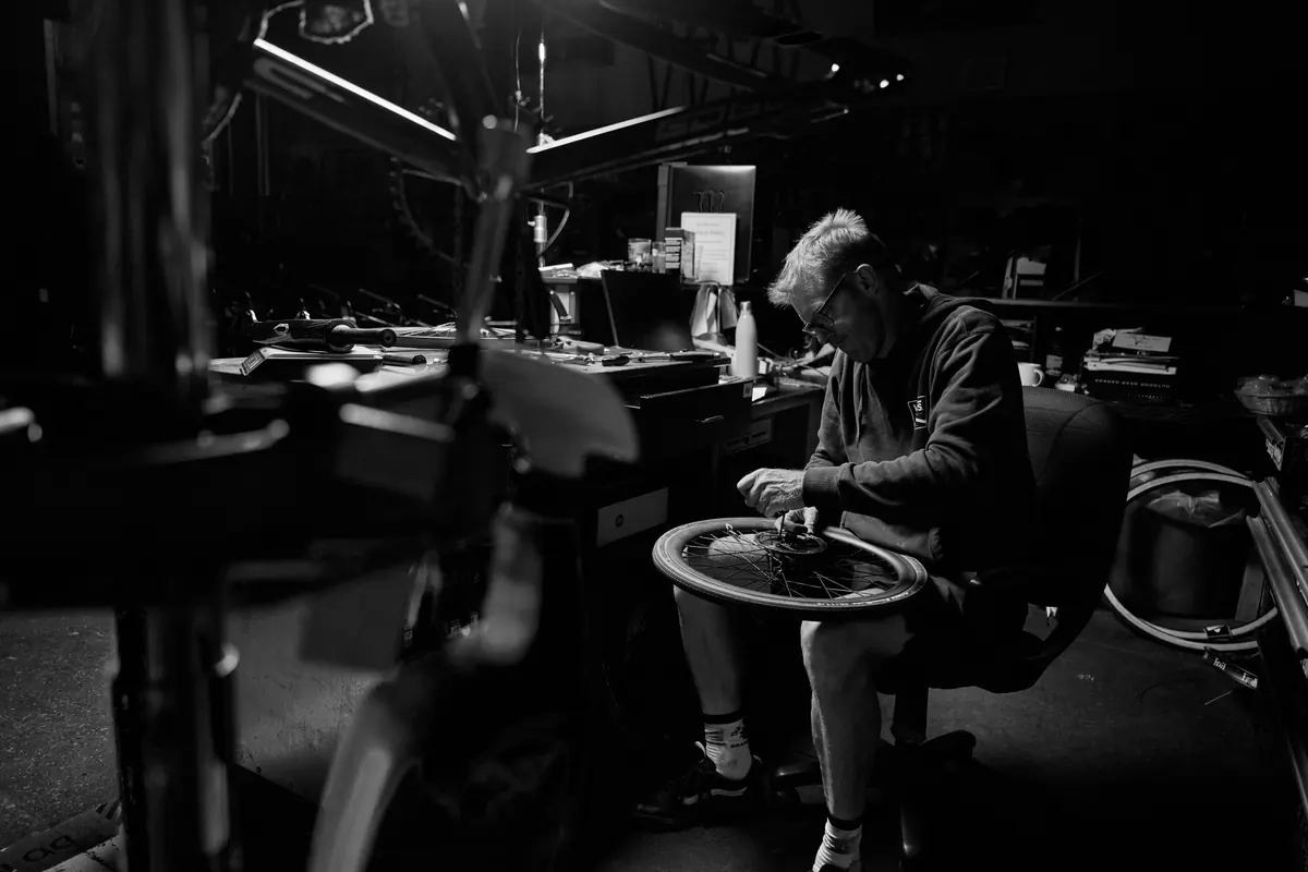 A bike-shop technician truing a wheel under workshop light at XKIDS Bike Service & Fit Check.